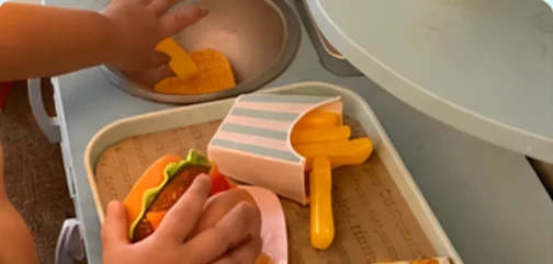 Little hands serving a play-food burger and fries on a toy tray